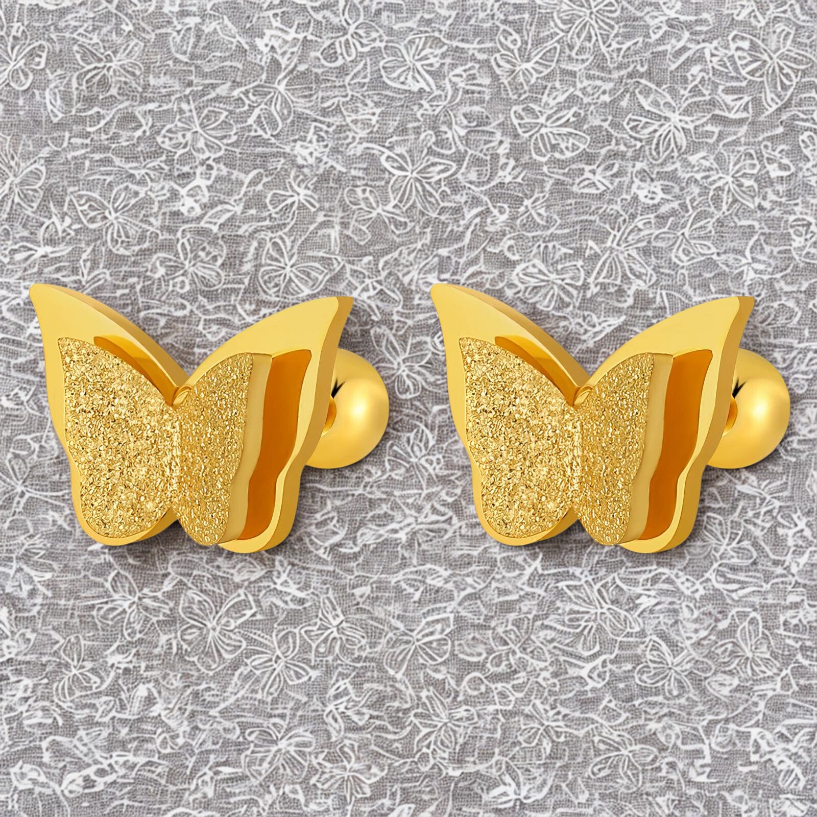 Gold butterfly-shaped earrings on a gray floral patterned background