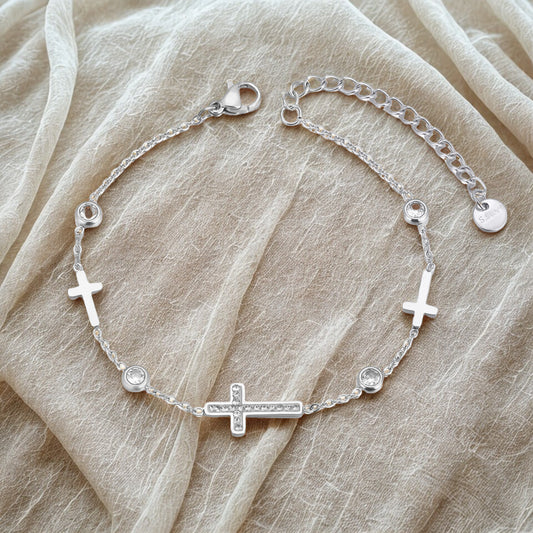 Silver bracelet with cross charms on a beige fabric background