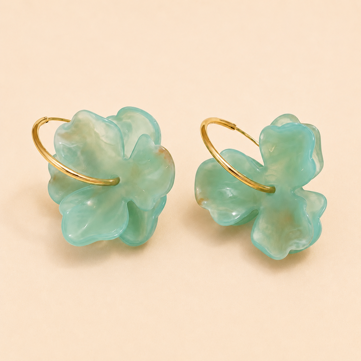 Pair of earrings with gold loops and green leaf-like designs on a beige background