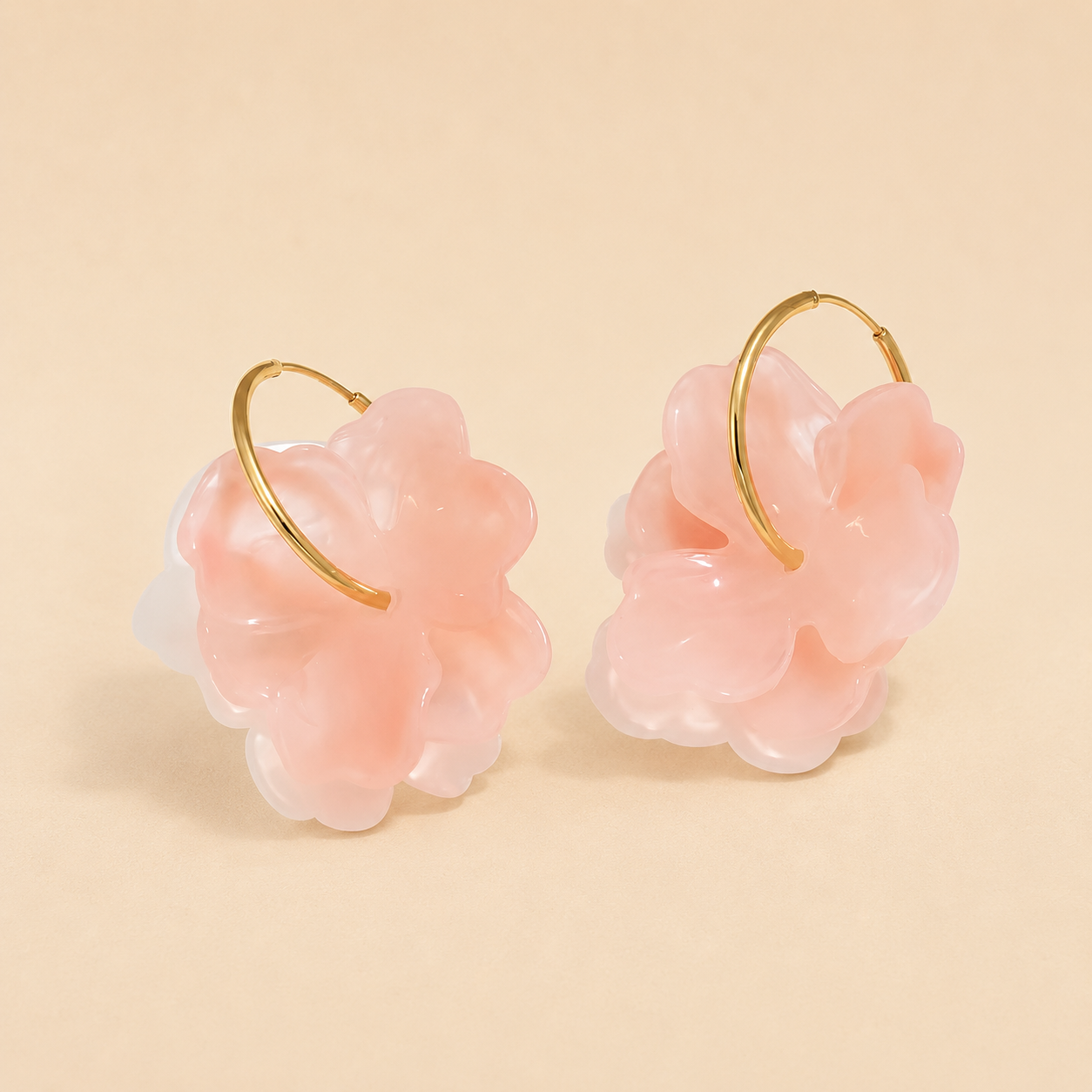 Pair of pink floral earrings with gold loops on a beige background