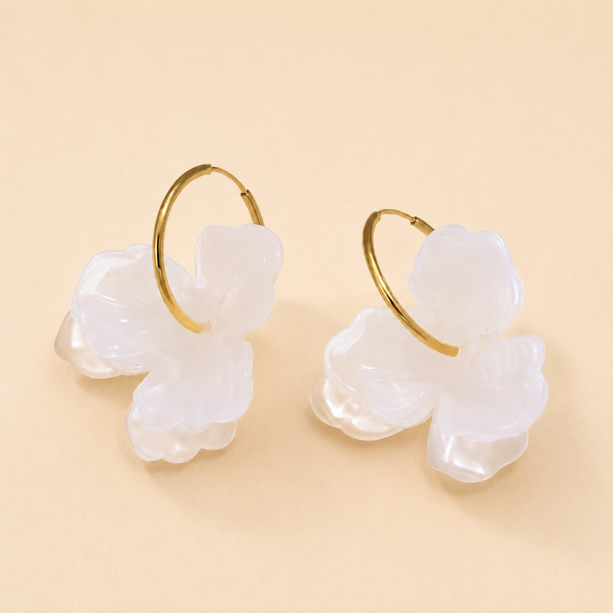 Pair of white floral earrings with gold hoops on a beige background