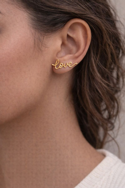Gold 'love' earring worn by a person with blurred background