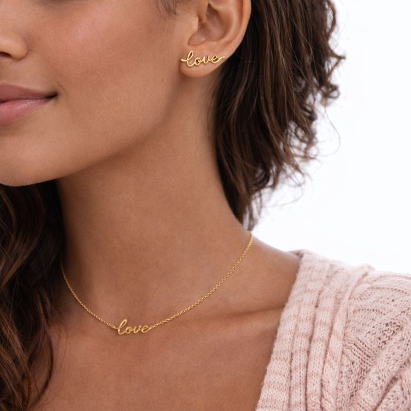 Gold 'love' necklace and earrings on a model with a blurred background