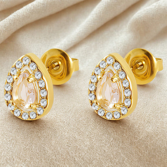 Gold earrings with teardrop-shaped gemstones on a beige fabric background