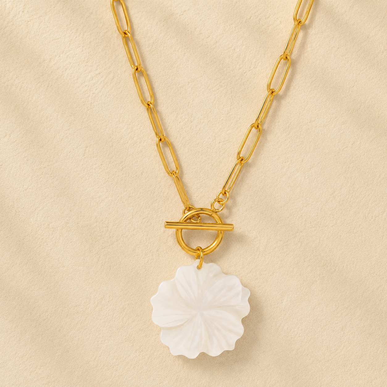 Gold chain necklace with a white floral pendant on a beige background