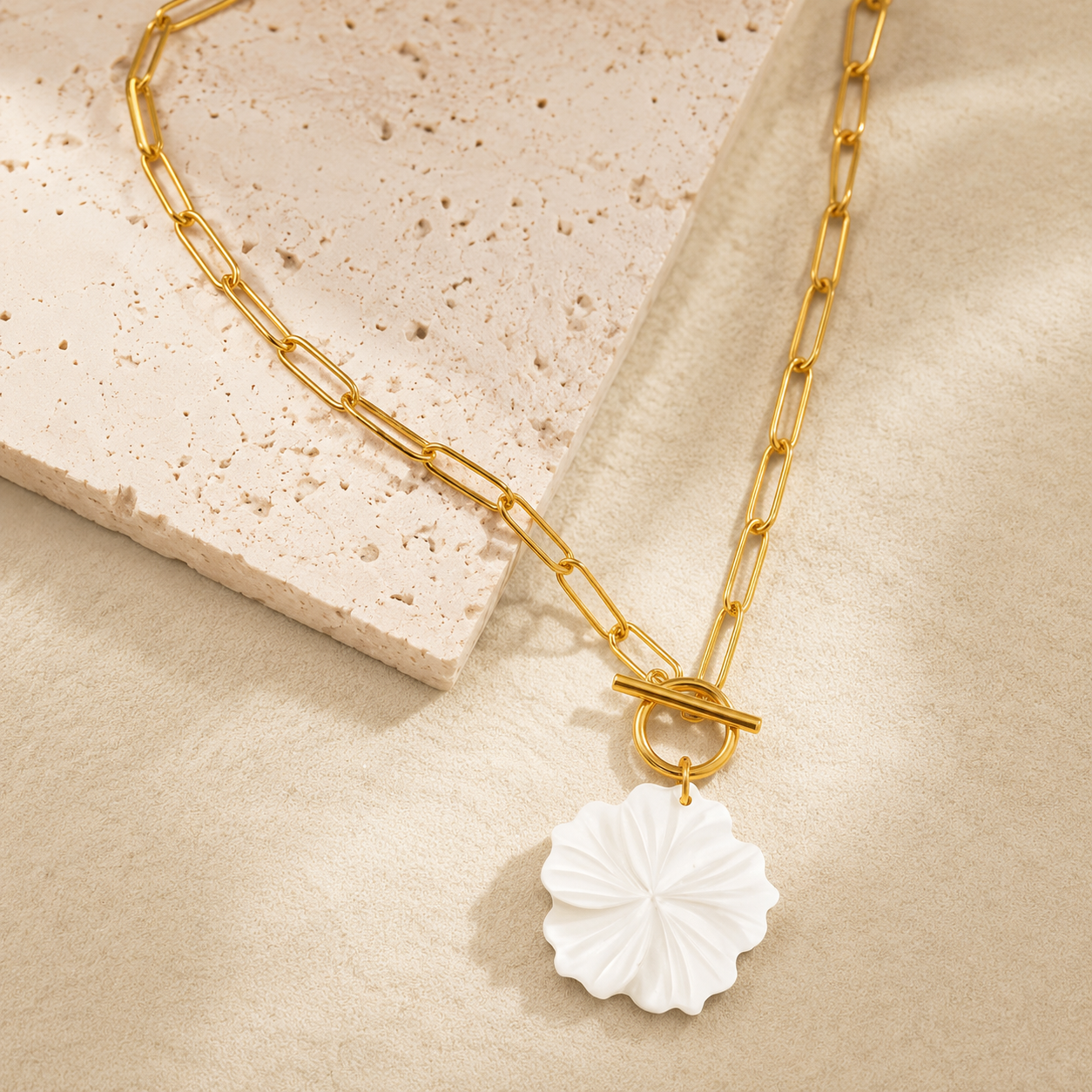 Gold necklace with a white floral pendant on a beige surface