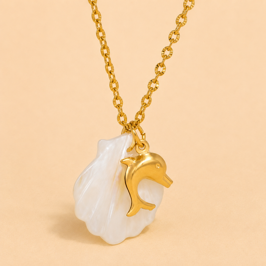 Gold necklace with a shell and dolphin pendant on a beige background