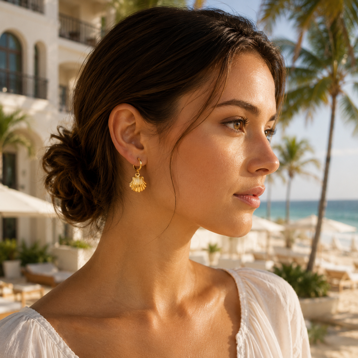 Woman wearing gold earrings with a beach and palm trees in the background