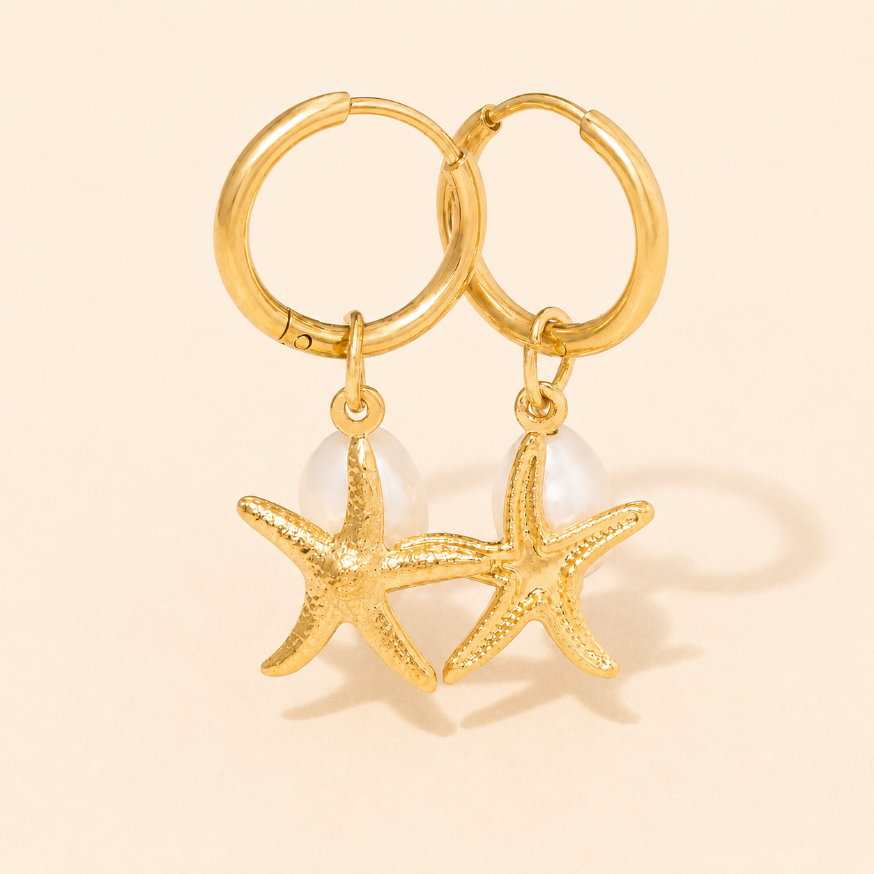Gold hoop earrings with starfish charms on a beige background