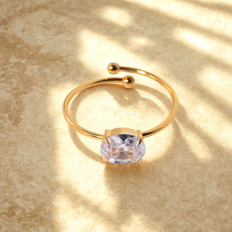 Gold ring with a clear gemstone on a beige surface