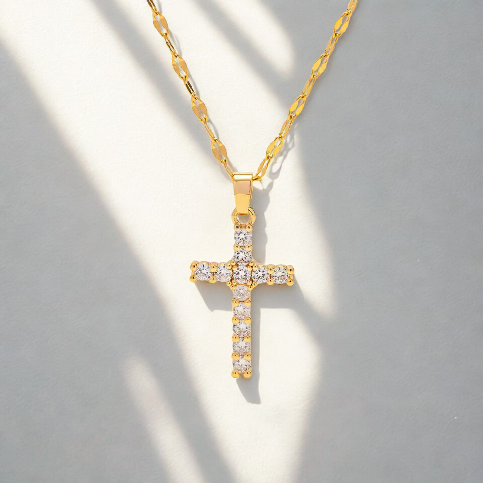 Gold cross necklace with clear stones on a gray background
