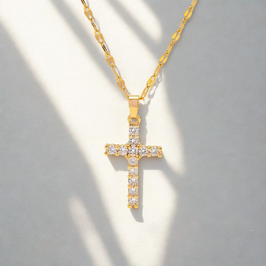 Gold cross necklace with clear stones on a gray background