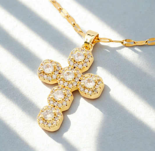 Gold cross necklace with clear stones on a light background
