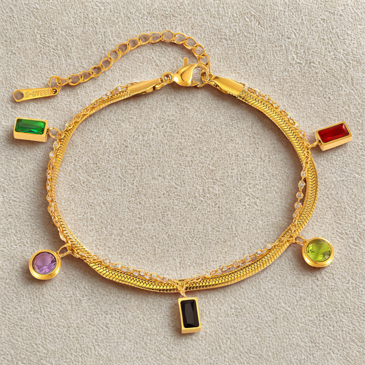 Gold bracelet with colorful gemstone charms on a light gray background