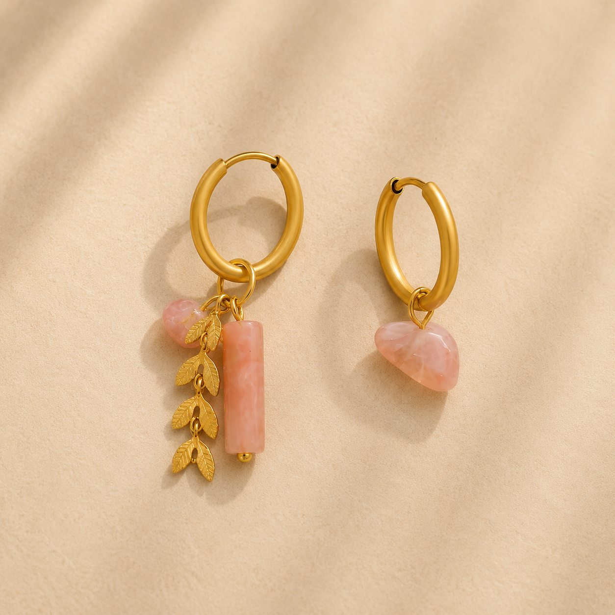 Gold asymmetrical hoop earrings with blush pink stone accents and delicate botanical leaf details.