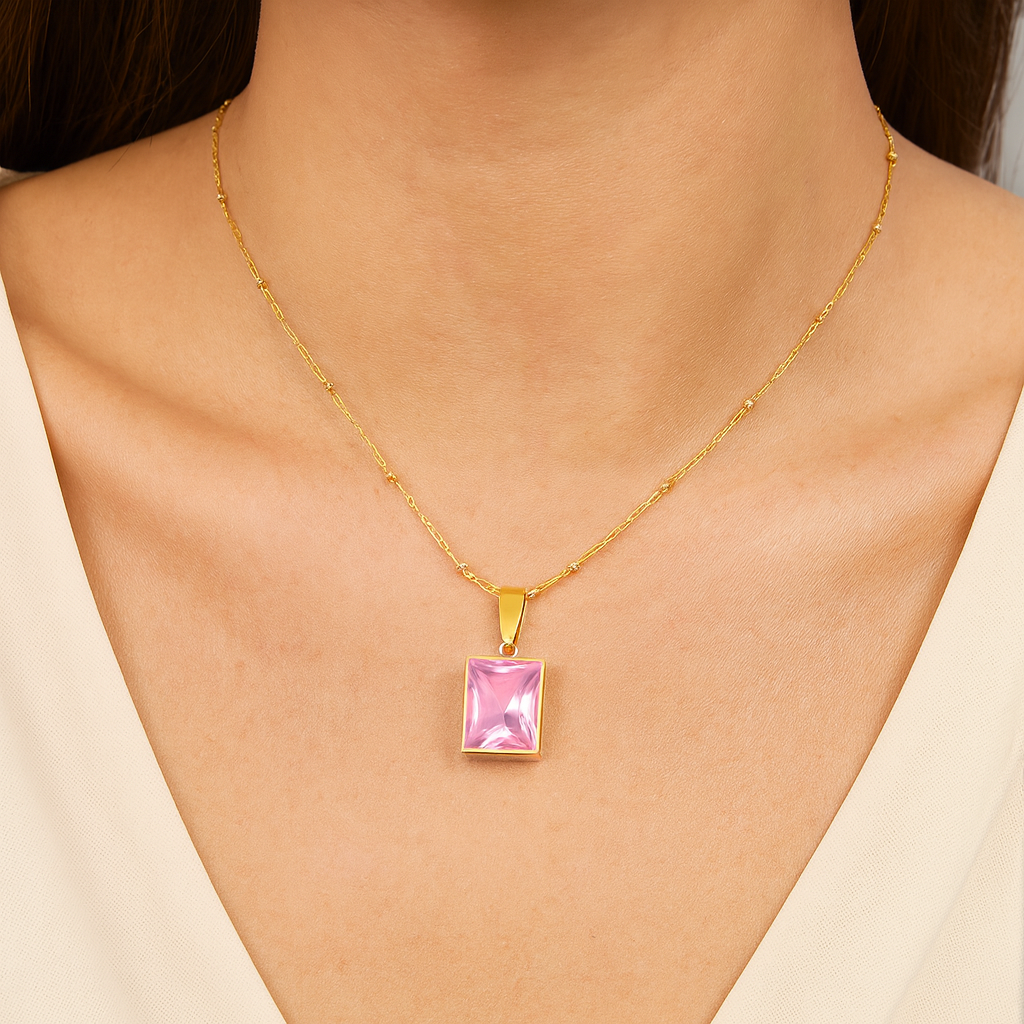 Gold necklace with a pink pendant on a model wearing a beige top.