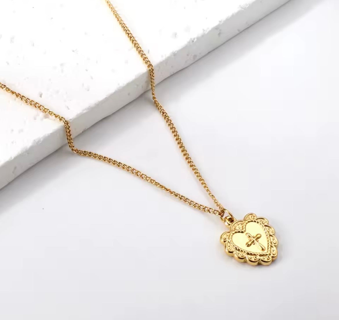 Gold necklace with a heart-shaped pendant with a cross on a white background