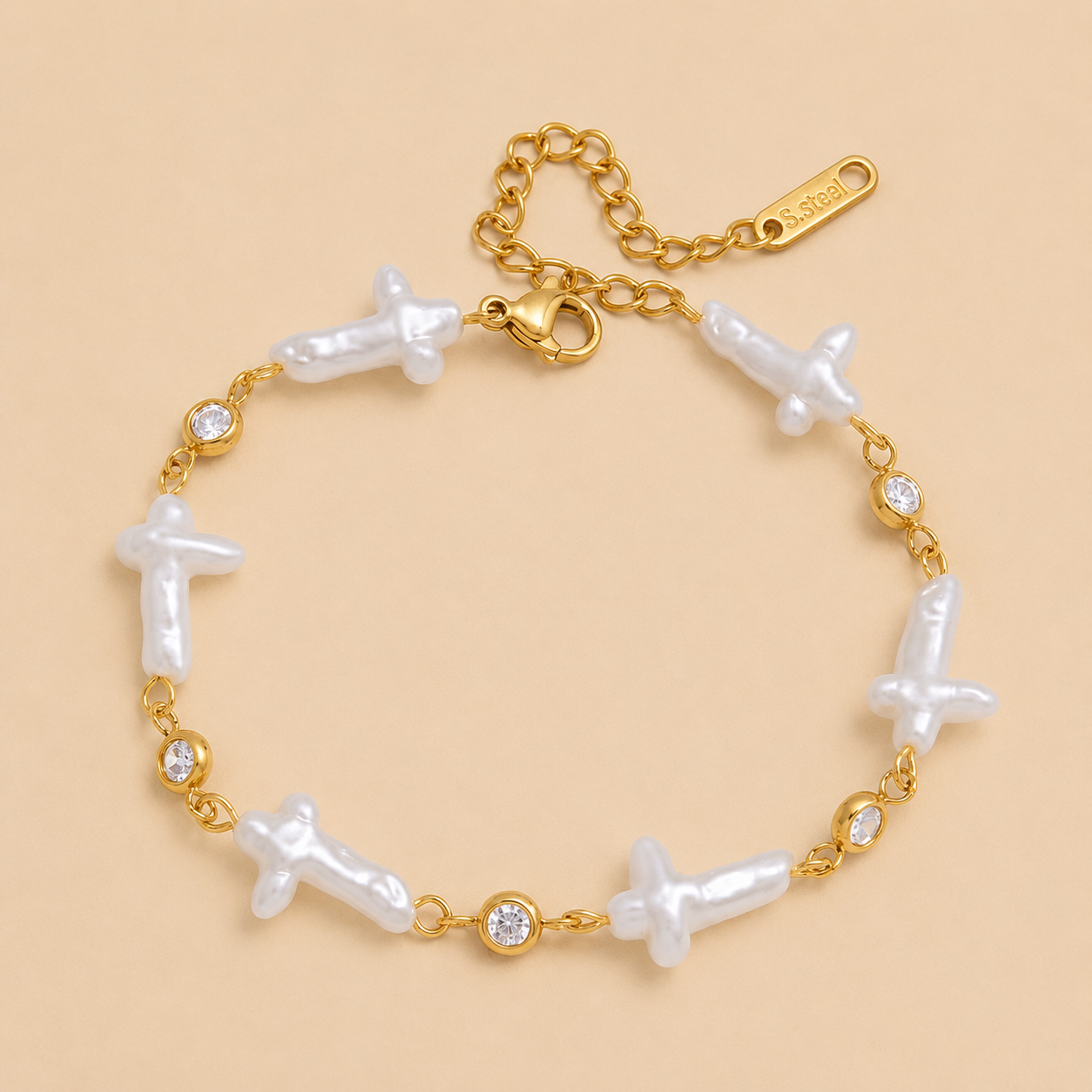 Gold bracelet with white pearl-like crosses on a beige background