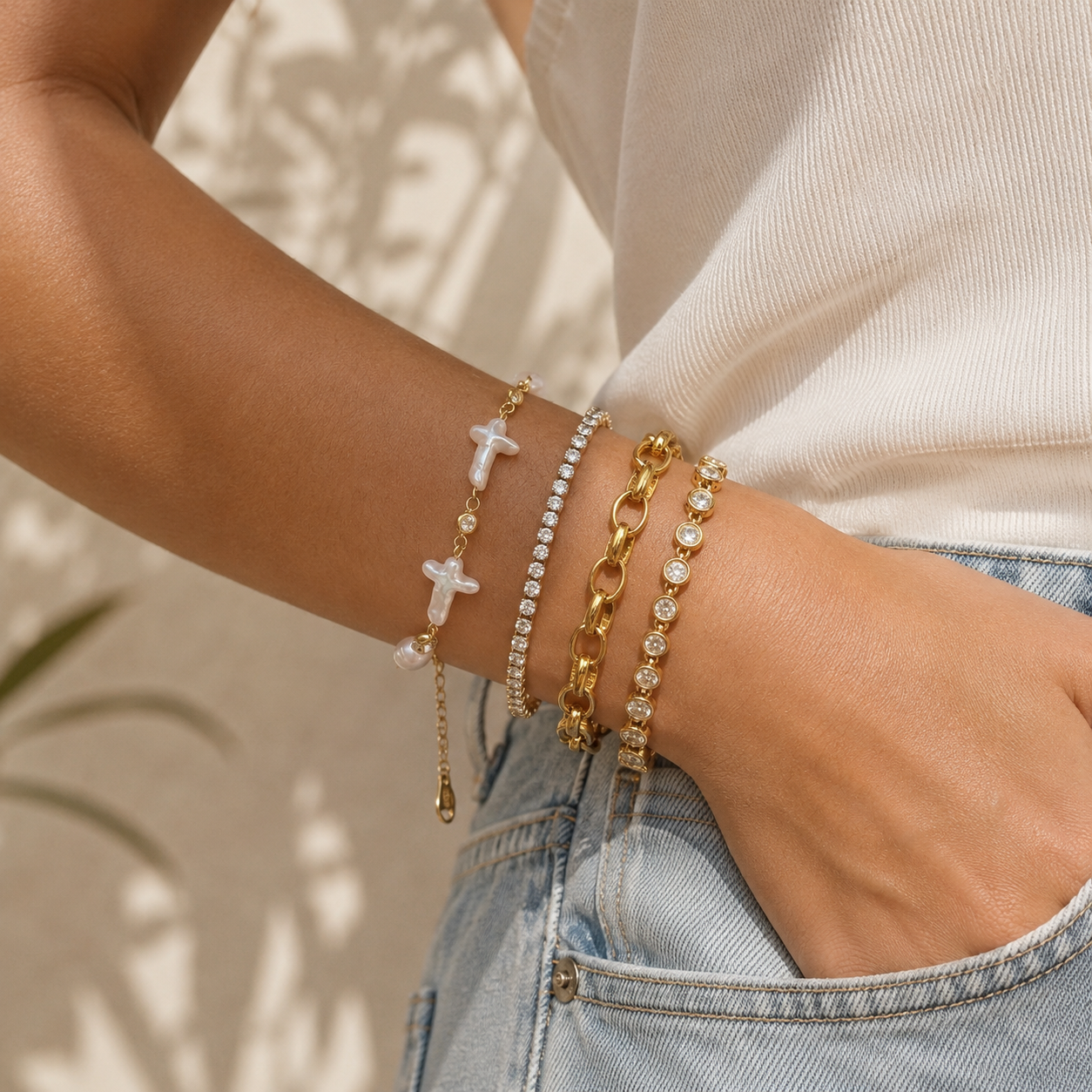 Close-up of a person's arm wearing multiple gold bracelets with crosses and pearls against a neutral background.