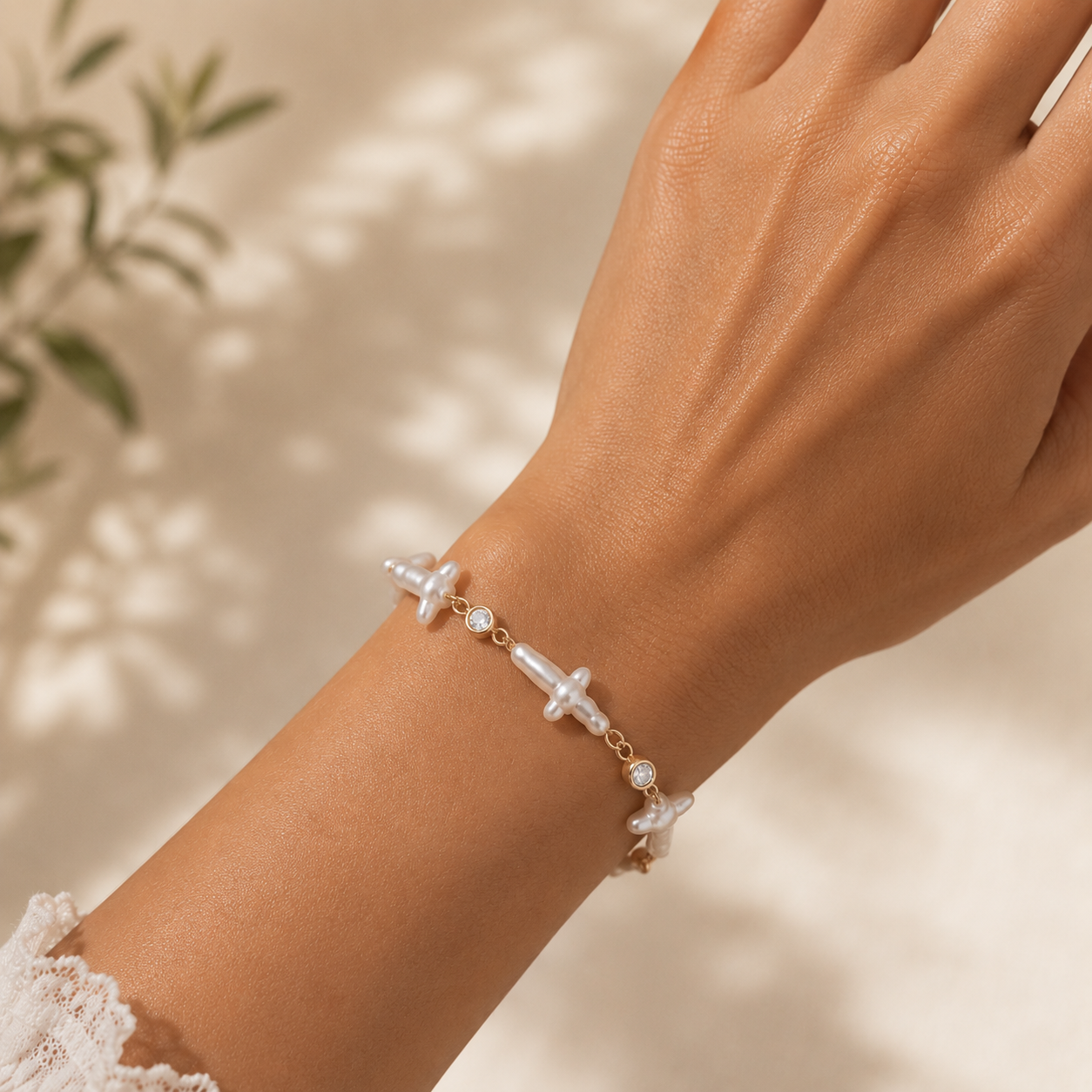 Hand wearing a delicate bracelet with pearl cross against a natural background