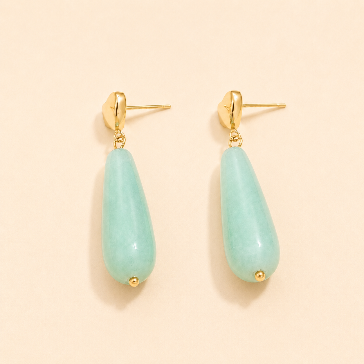 Teardrop-shaped aqua marine blue green earrings with gold accents on a beige background