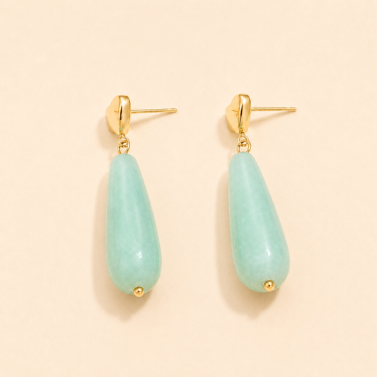 Teardrop-shaped aqua marine blue green earrings with gold accents on a beige background