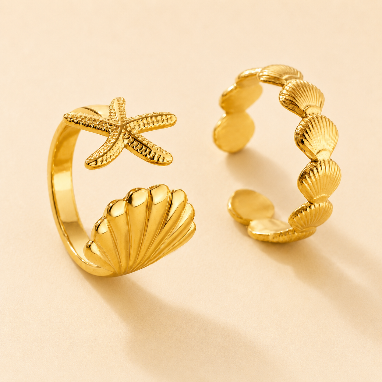 Two gold rings with starfish and shell designs on a beige background