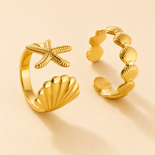 Two gold rings with starfish and shell designs on a beige background