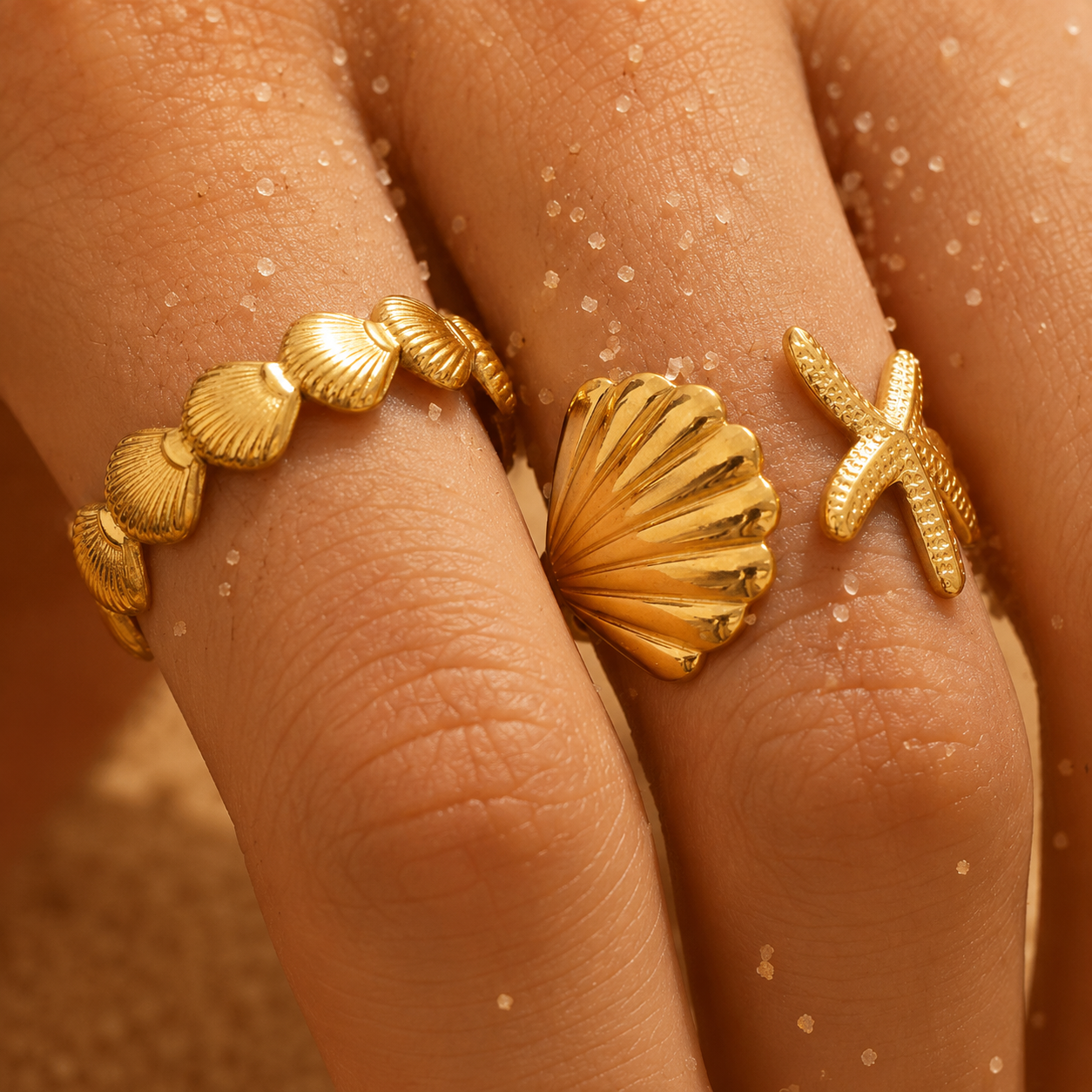 Close-up of a hand wearing two gold rings with shell and starfish designs.