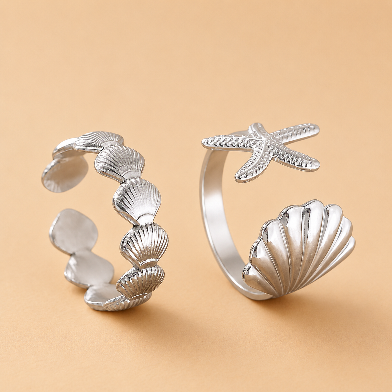 Silver open rings with shell and starfish designs on a beige background