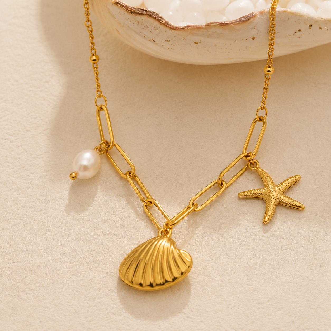 Gold necklace with shell, starfish, and pearl pendant on a beige background