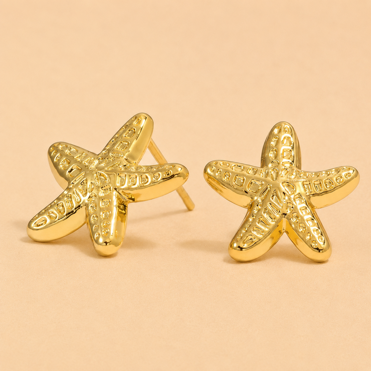 Gold starfish earrings on a beige background