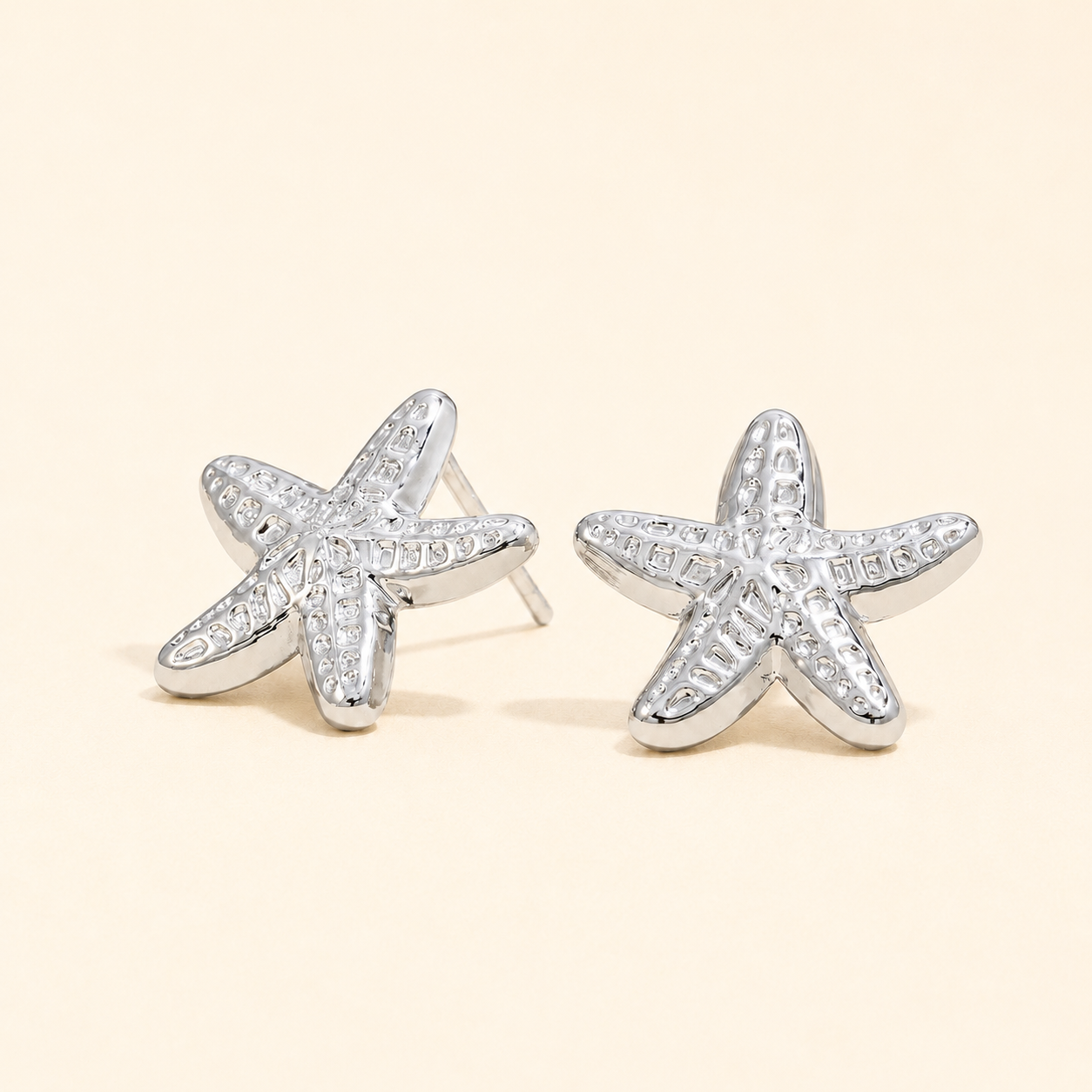 Starfish-shaped silver earrings with clear stones on a beige background