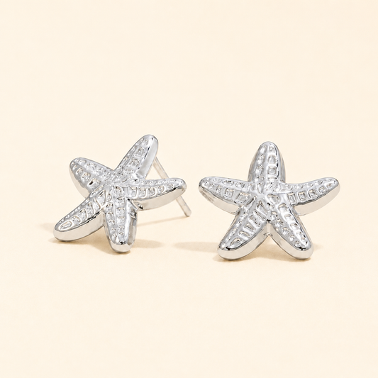 Starfish-shaped silver earrings with clear stones on a beige background