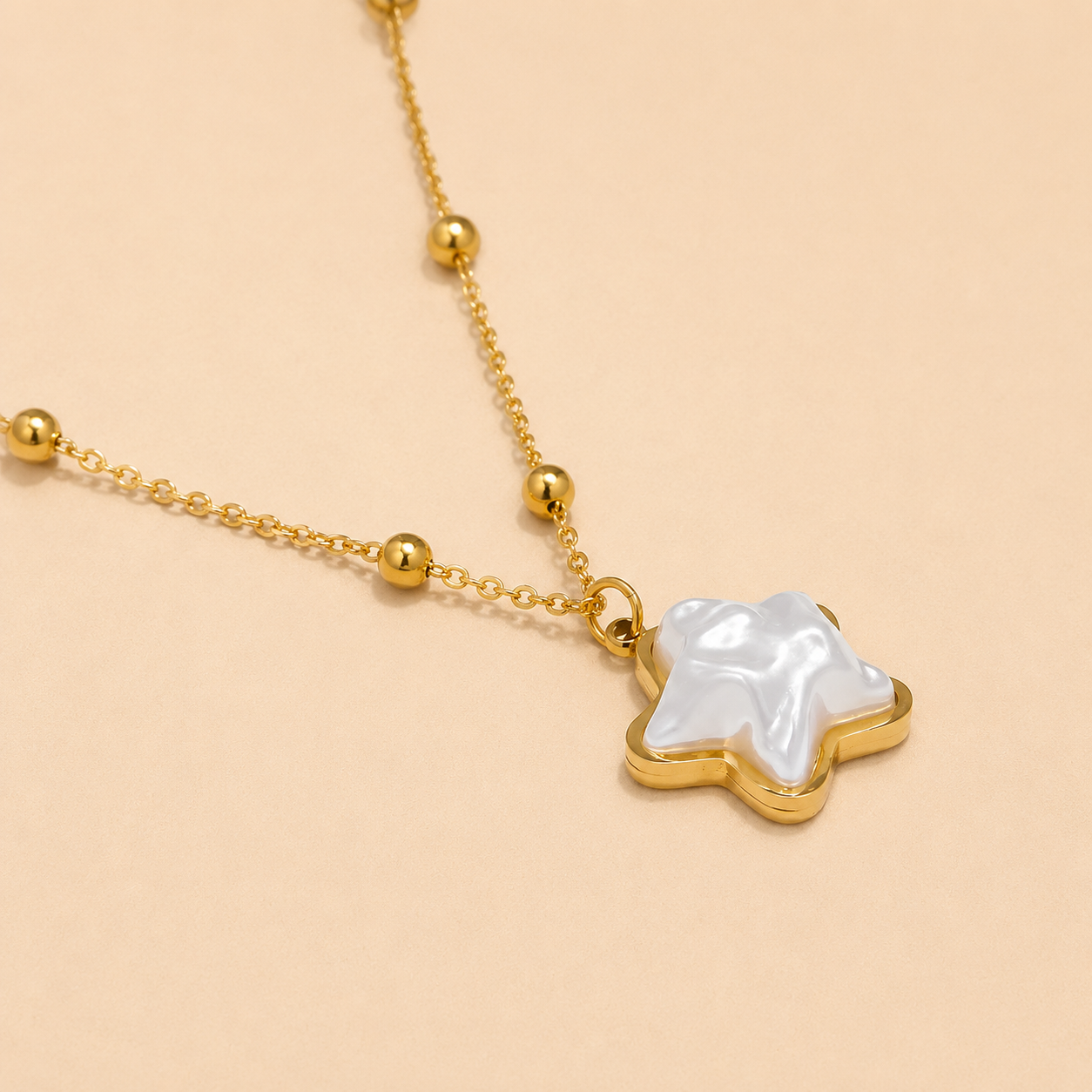 Gold necklace with a star-shaped pendant featuring a white pearl on a beige background