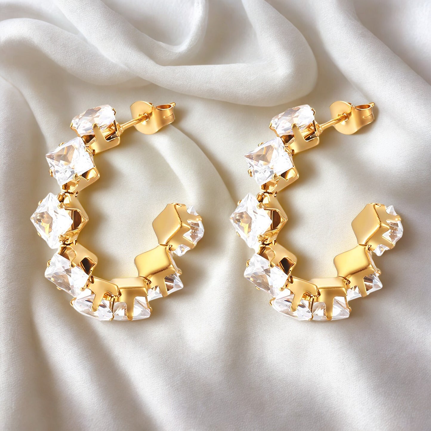 Gold hoop earrings with clear gemstones on a white fabric background