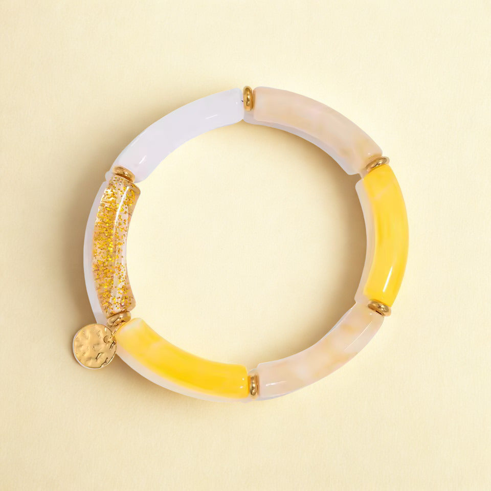 Multicolored bracelet with yellow, white, and gold segments on a beige background