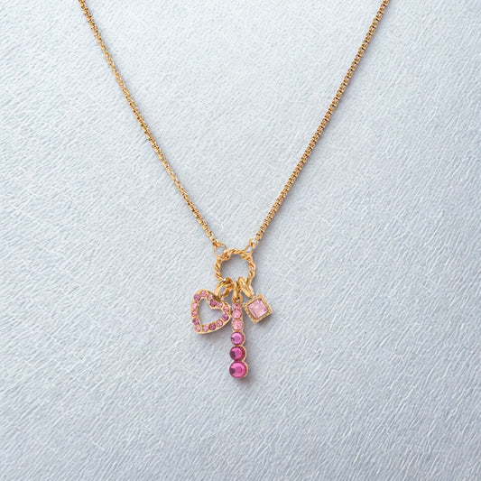 Gold necklace with pink heart and key charm on a light gray background