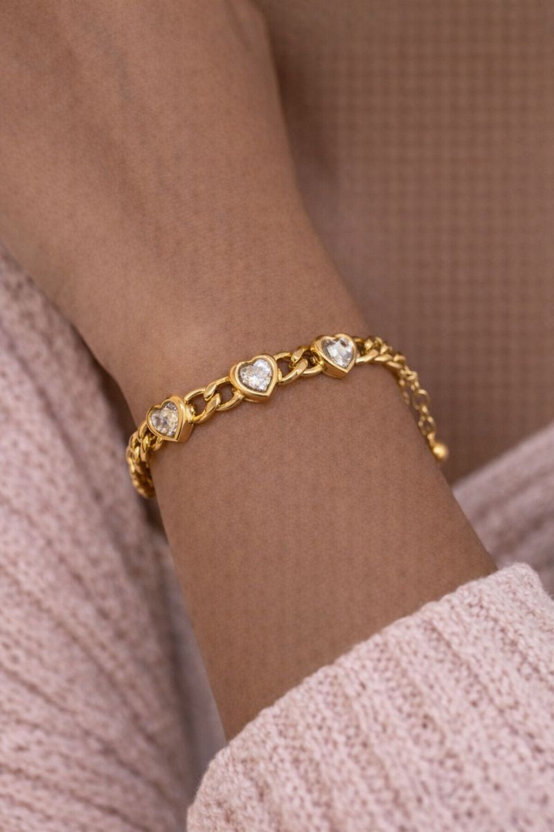 Gold bracelet with heart-shaped charms on a wrist against a neutral background