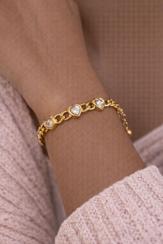Gold bracelet with heart-shaped charms on a wrist against a neutral background