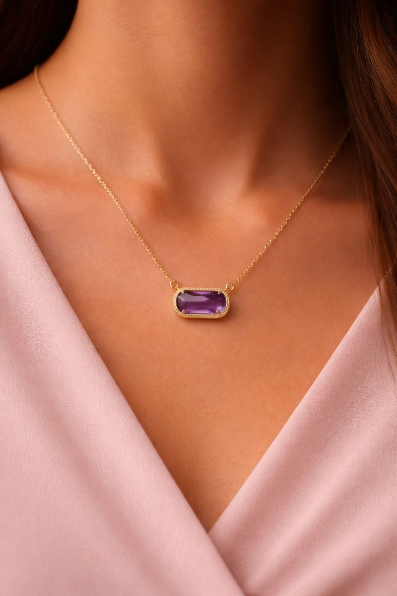 Gold necklace with a purple gemstone pendant on a person wearing a pink top.