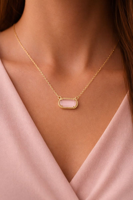 Gold necklace with a pink pendant on a person wearing a pink top.