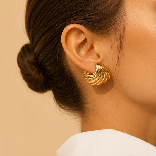 Gold shell earrings worn by a person with a neutral background