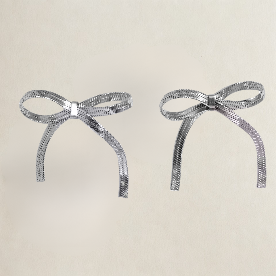 Two silver bow-shaped earrings on a beige background