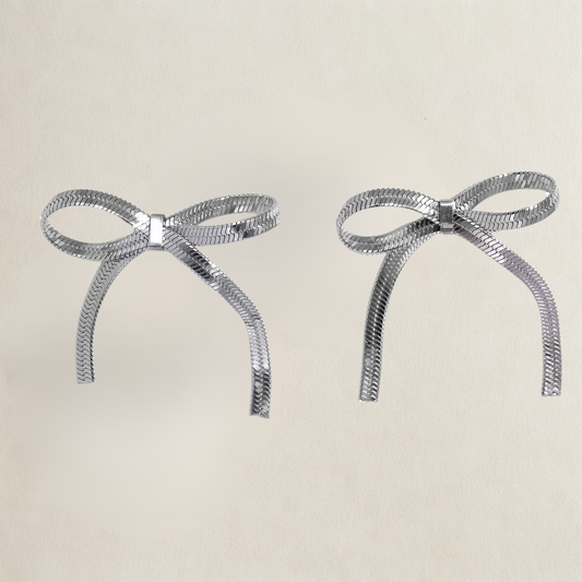 Two silver bow-shaped earrings on a beige background