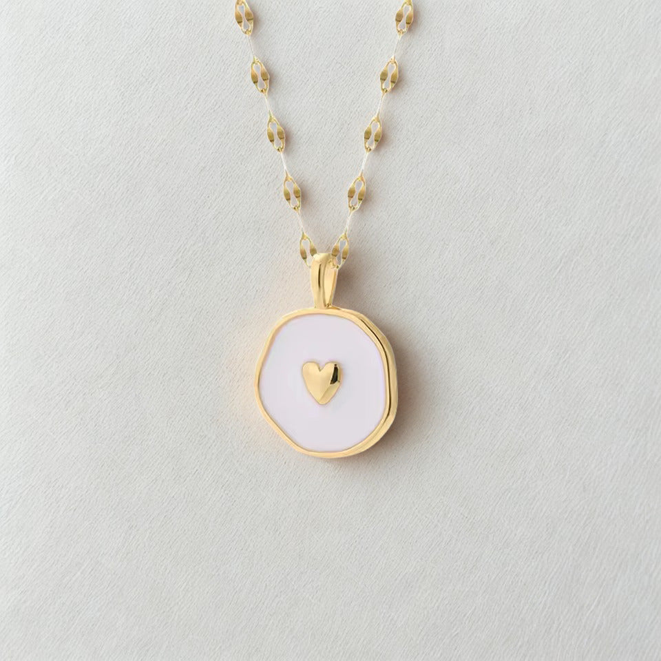 Gold necklace with a white pendant featuring a heart on a light gray background