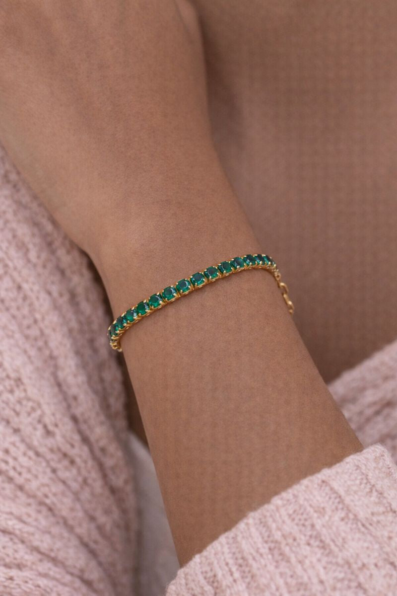 Gold bracelet with green gemstones on a wrist against a neutral background
