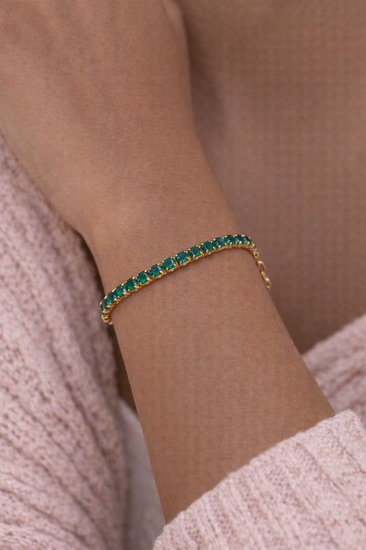 Gold bracelet with green gemstones on a wrist against a neutral background